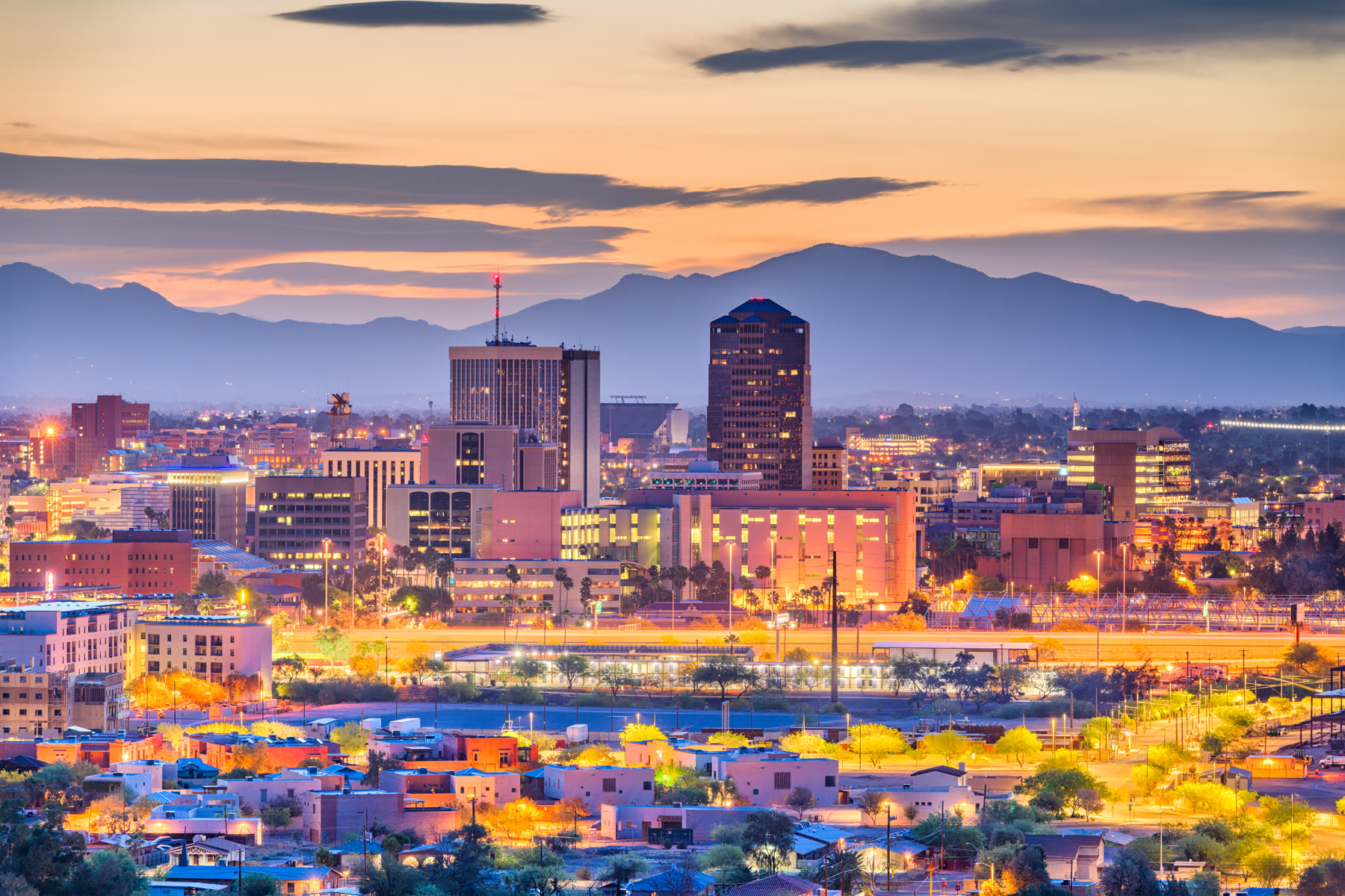 Downtown Tucson glowing at dusk, mountain ranges rising behind the city.